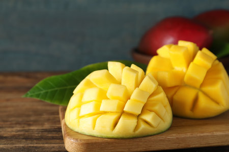 Halves of ripe mango cut into cubes on wooden tableの写真素材