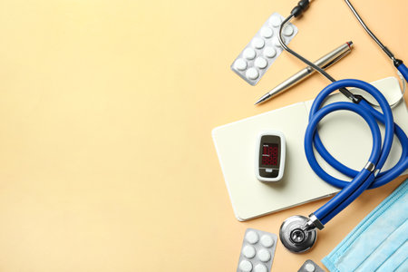 Flat lay composition with fingertip pulse oximeter and medical items on orange background. Space for...