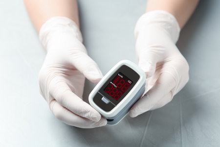 Doctor in gloves holding fingertip pulse oximeter at light gray table, closeupの写真素材