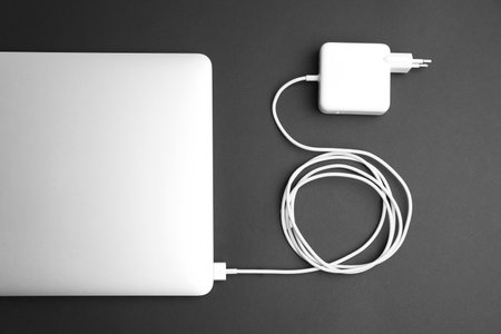 Laptop and charger on black background, flat lay. modern technologyの写真素材