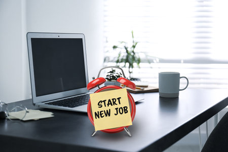 Sticker with text Start New Job on alarm clock near laptop in modern officeの写真素材