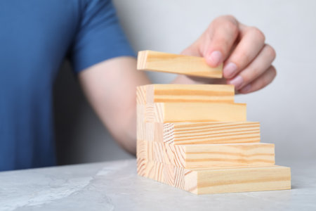 Man building steps with wooden blocks on light gray marble table, closeup. Career ladderの写真素材
