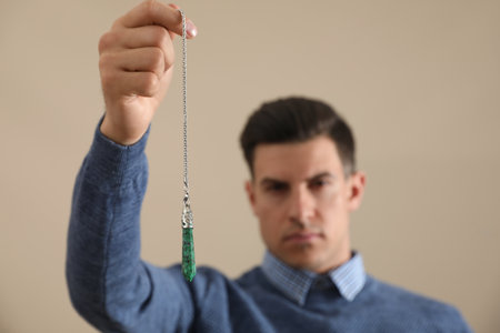 Psychotherapist with pendulum on beige background. Hypnotherapy sessions