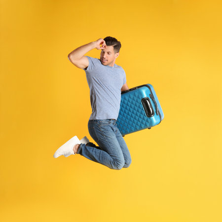 Handsome man with suitcase for summer trip jumping on yellow background. vacation travelの写真素材