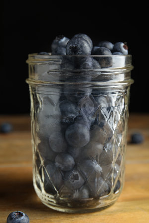 Tasty ripe blueberries in glass jar on wooden tableの写真素材