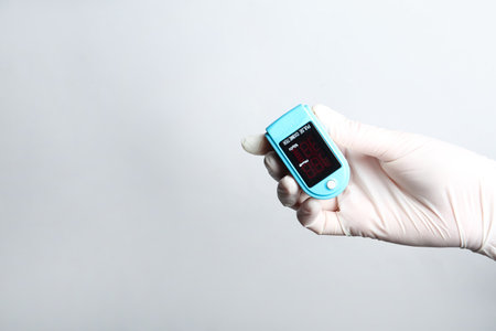 Doctor in gloves holding fingertip pulse oximeter on white background, closeup. Space for textの写真素材