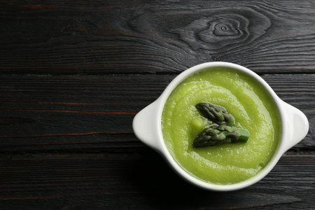 Delicious asparagus soup in bowl on black wooden table, top view. Space for textの写真素材