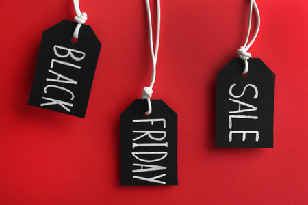 Tags with words BLACK FRIDAY SALE hanging on red backgroundの写真素材