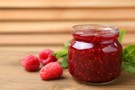 Delicious jam and fresh raspberries on wooden table, closeup. Space for text