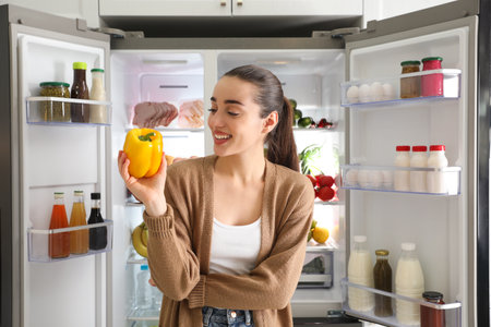Young woman with bell pepper near open refrigeratorの写真素材