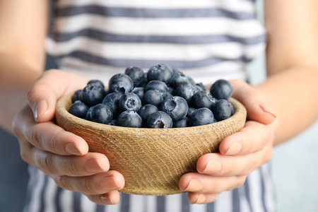 Woman holding fresh ripe blueberries in wooden bowl, closeupの写真素材