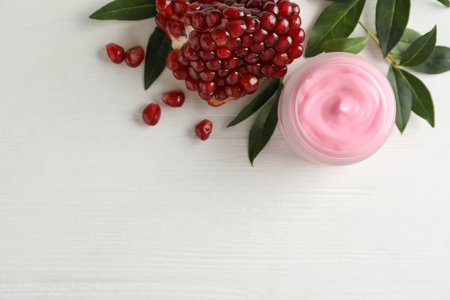 Jar with natural facial mask, pomegranate seeds and green leaves on white wooden table, flat lay. Space for textの写真素材