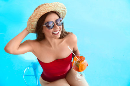 Woman with glass of refreshing drink in swimming pool