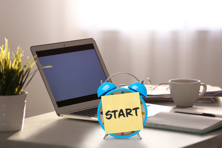 new job. Sticker with word Start on alarm clock near laptop in modern office