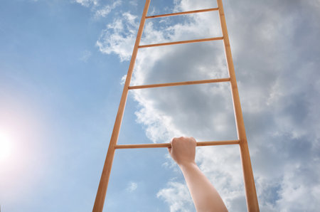 Woman climbing up wooden ladder against blue sky with clouds, closeupの写真素材