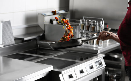 Woman cooking tasty food on stove in restaurant kitchen, closeupの写真素材