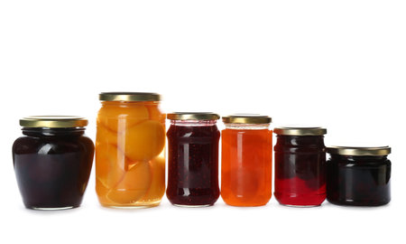 Glass jars with different pickled fruits and jams on white backgroundの写真素材