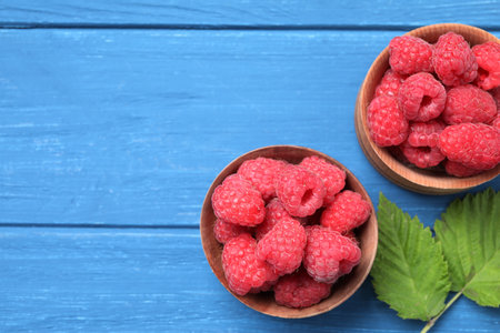 Delicious fresh ripe raspberries on blue wooden table, flat lay. Space for text