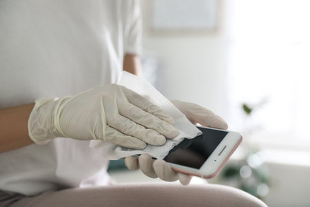 Woman cleaning mobile phone with wet wipe indoors, closeupの写真素材