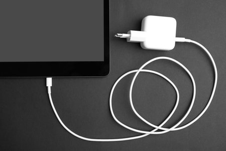 Tablet and USB charger on black background, flat lay. modern technology