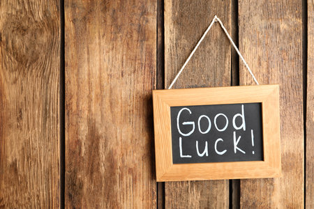 Blackboard with phrase GOOD LUCK hanging on wooden wall. Space for textの写真素材