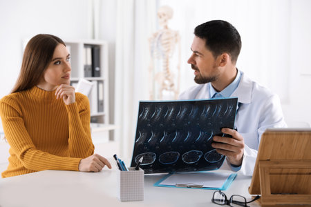 Orthopedist showing X-ray picture to patient at table in clinicの写真素材
