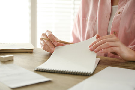 Woman with pencil and notepad at wooden table, closeup
