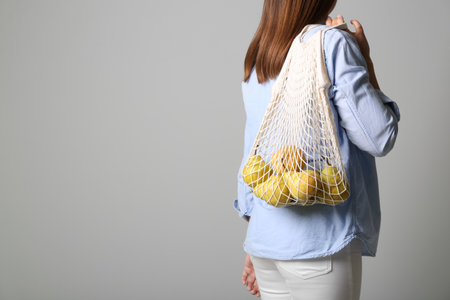 Woman holding net bag with fresh ripe pears on gray background, closeup. Space for textの写真素材