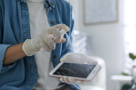Woman applying antibacterial spray onto smartphone indoors, closeupの写真素材