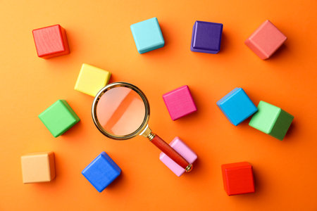 Different colorful cubes and magnifier glass on orange background, flat lay. Find keywords conceptの写真素材