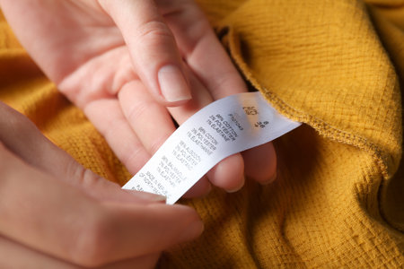 Woman reading clothing label with size and content information on yellow garment, closeupの写真素材