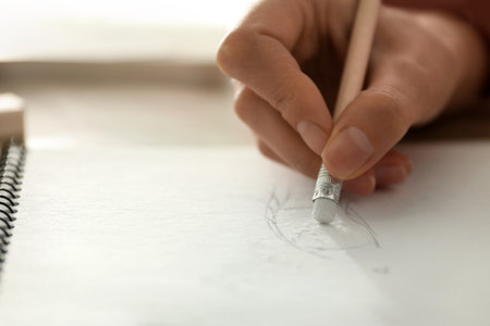 Woman correcting picture in notepad with pencil eraser at table, closeup