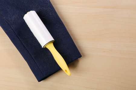 Lint roller and sleeve of jacket covered with hair on wooden table, flat lay. Space for textの写真素材