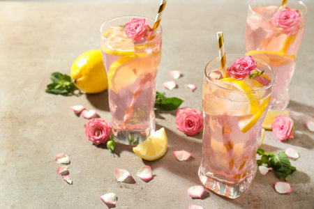 Delicious refreshing drink with rose flowers and lemon slices on light gray tableの写真素材