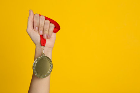 Woman holding gold medal on yellow background, closeup. space for designの写真素材