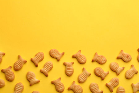 Delicious goldfish crackers on yellow background, flat lay. Space for textの写真素材