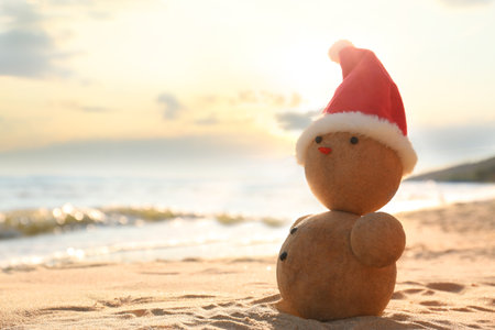 Snowman made of sand with Santa hat on beach near sea, space for text. christmas holidaysの写真素材