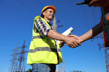 Professional electricians shaking hands near high voltage tower, closeupの写真素材