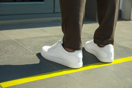 Man standing on taped floor marking for social distance outdoors, closeup.