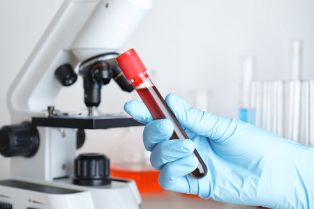 Scientist holding test tube with blood sample near microscope, closeup. laboratory analysisの写真素材