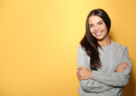 Happy young woman wearing warm sweater on yellow background. Space for textの写真素材