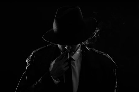 Old fashioned detective smoking cigarette on dark background, black and white effectの写真素材
