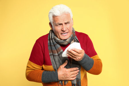 Senior man coughing on yellow background. Cold symptomsの写真素材