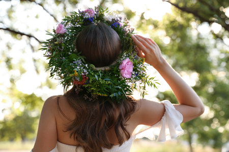 Young woman wearing wreath made of beautiful flowers outdoors on sunny day, back viewの写真素材