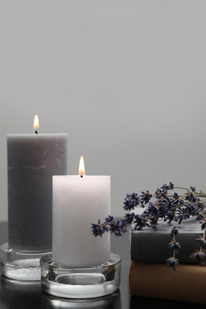 Wax candles in glass holders near books and lavender flowers on table against light backgroundの写真素材