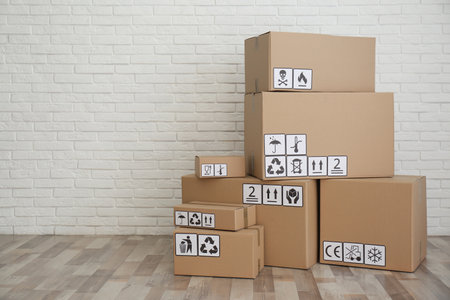 Cardboard boxes with different packaging symbols on floor near white brick wall, space for text. Parcel deliveryの写真素材