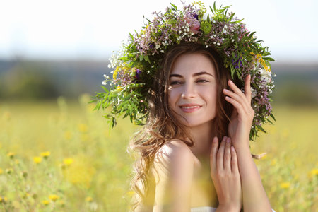 Young woman wearing wreath made of beautiful flowers in field on sunny dayの写真素材