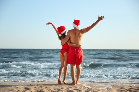 Lovely couple with Santa hats together on beach, back view. Christmas vacationの写真素材