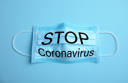 Medical mask with text Stop Coronavirus on light blue background. Protective measures during pandemicの写真素材