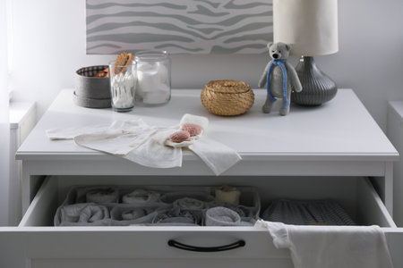 Modern open chest of drawers with baby clothes and accessories in the roomの写真素材